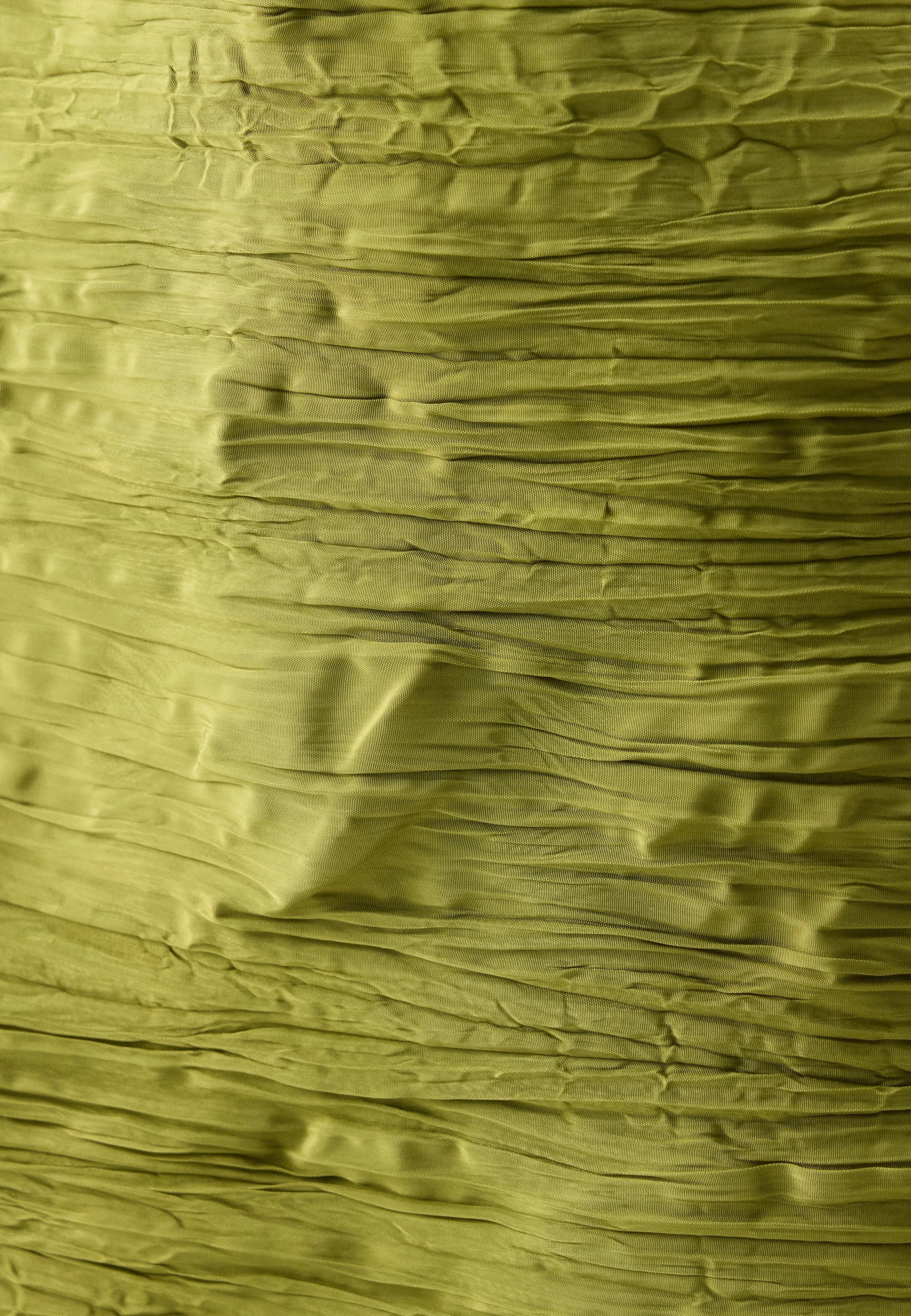 A close-up of olive green crinkled paper or textured fabric with horizontal folds and a slightly translucent surface.