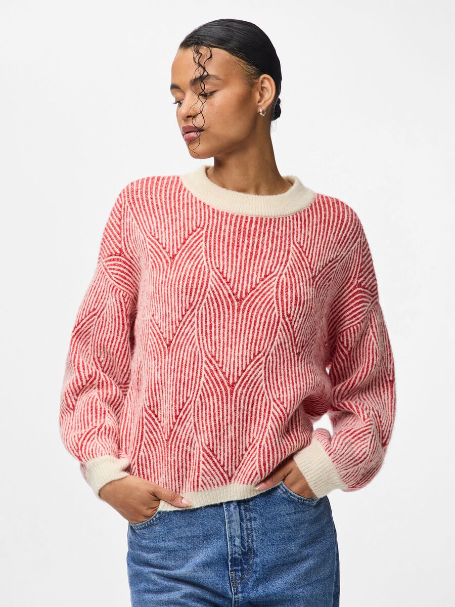 Person wearing a red and white patterned sweater with blue jeans on a plain background