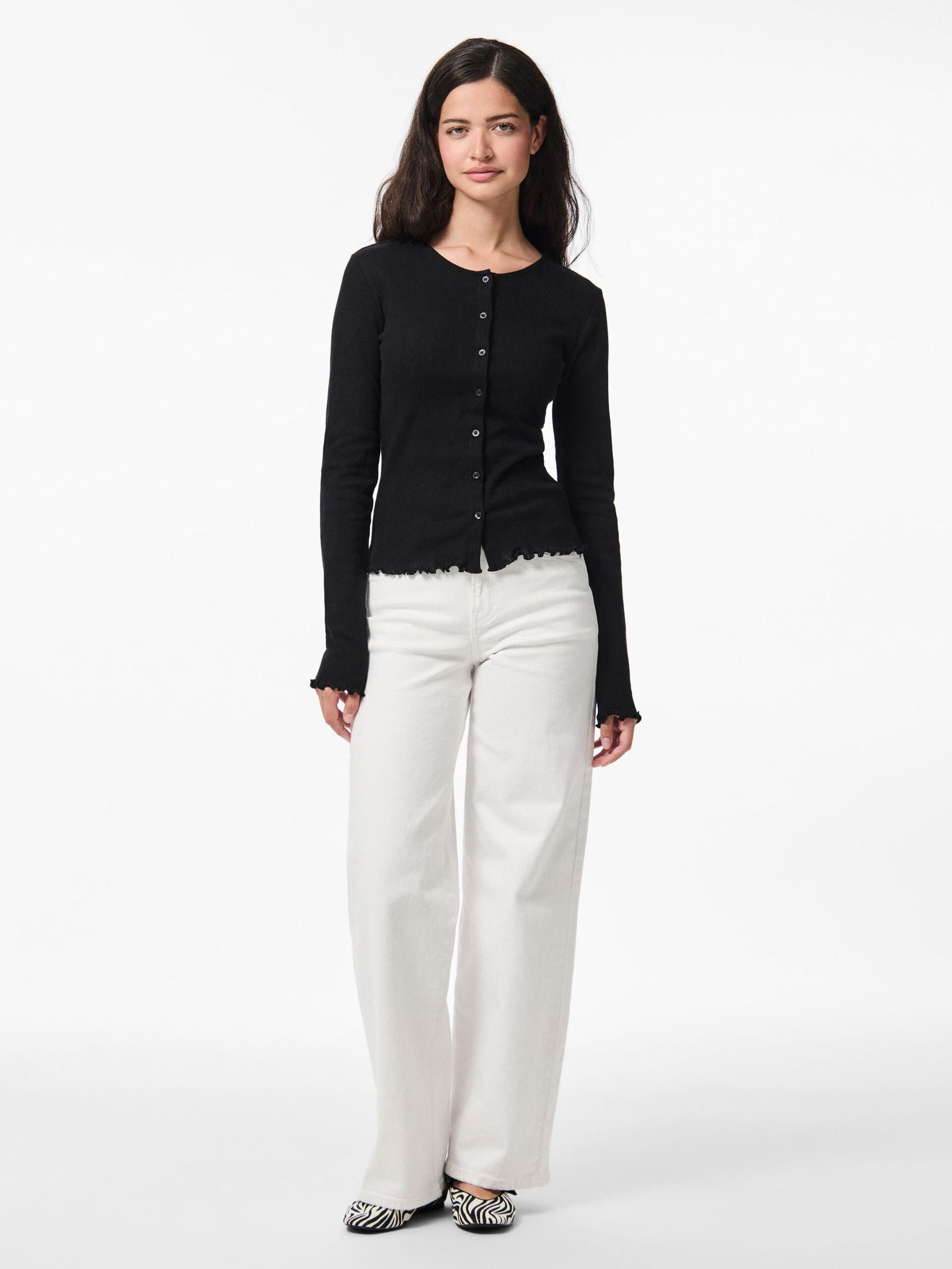 Woman wearing a black cardigan and white pants on a white background
