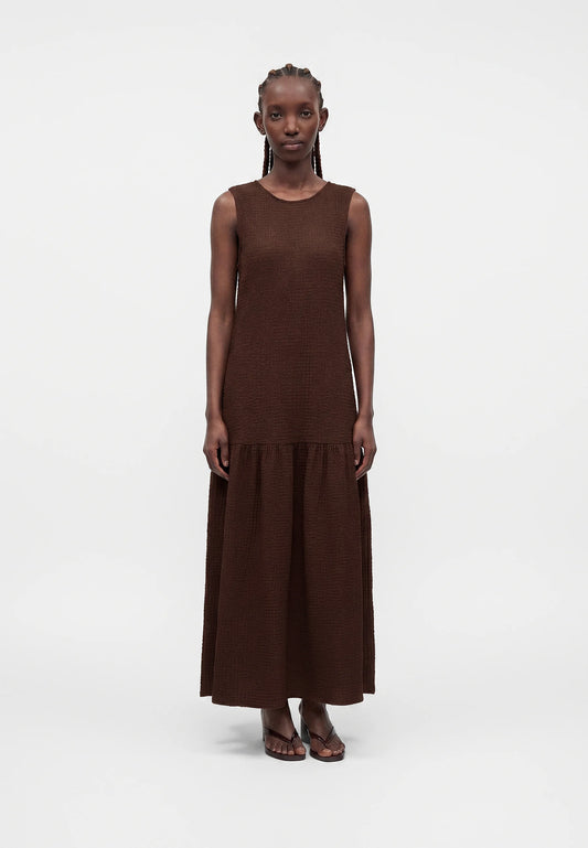 Person wearing a brown dress with a plain white background