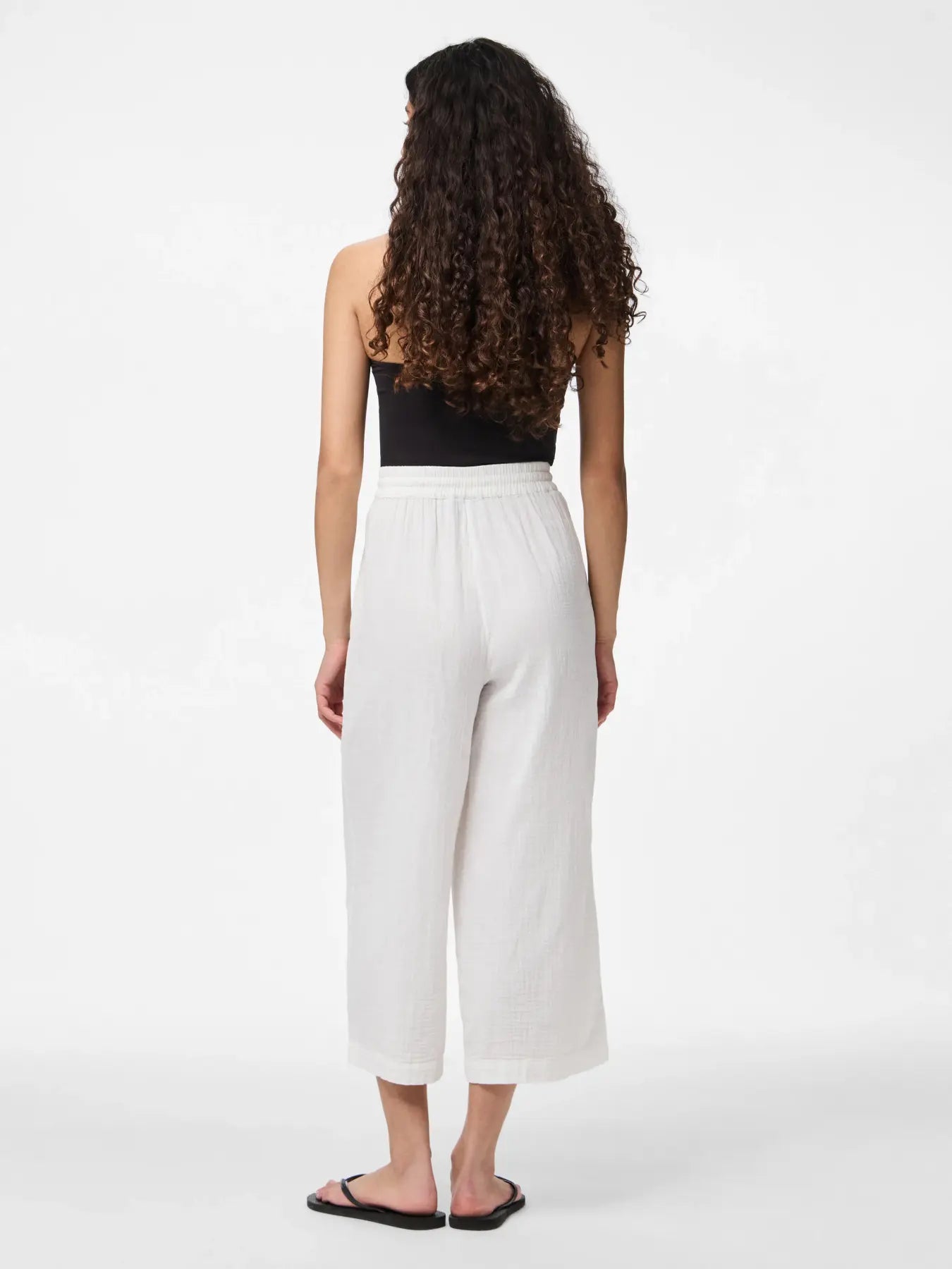 Woman wearing a black top and white pants on a white background