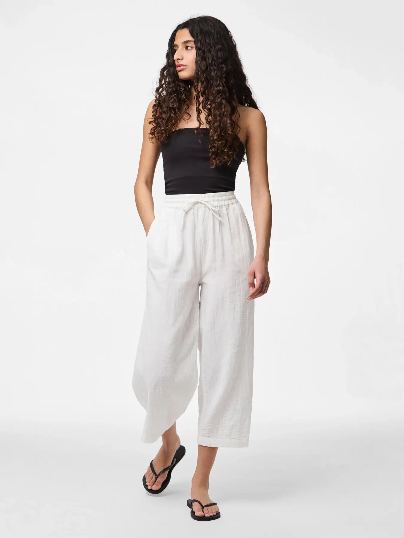 Woman wearing a black top and white wide-leg pants on a white background
