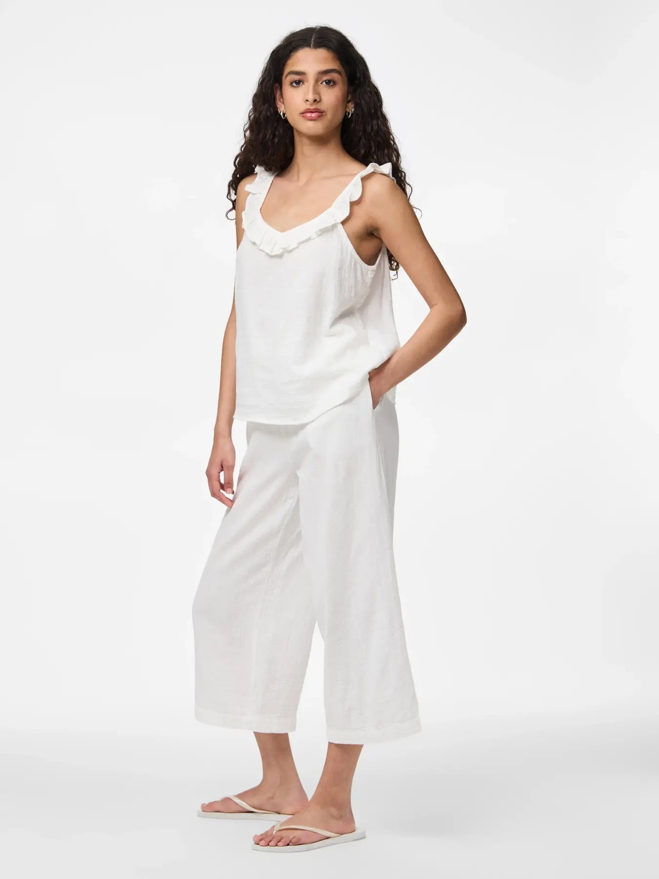 Woman wearing a white sleeveless top and pants on a white background