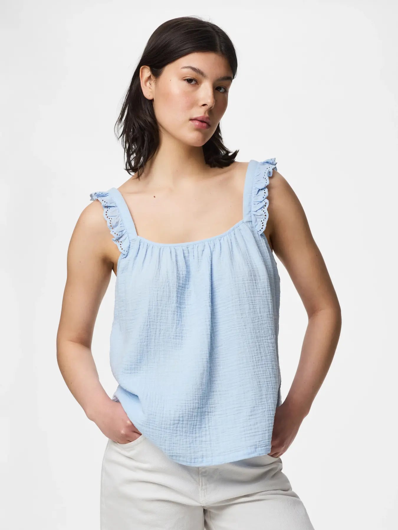 Woman wearing a light blue sleeveless top with ruffled straps on a white background