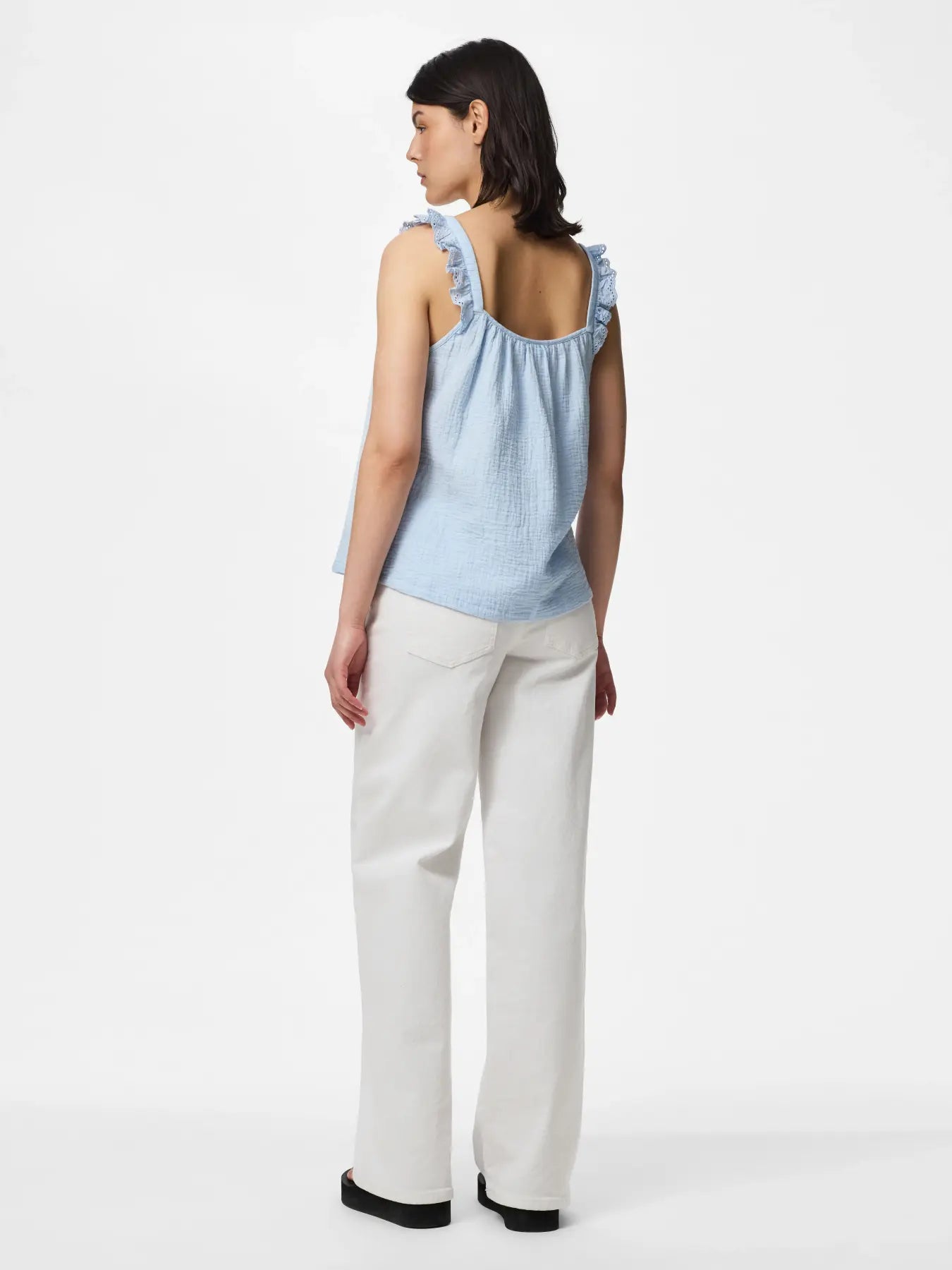 Woman wearing a light blue sleeveless top and white pants on a white background