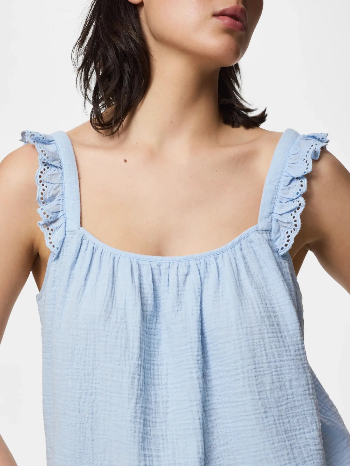 Light blue sleeveless top with ruffled straps worn by a person on a white background