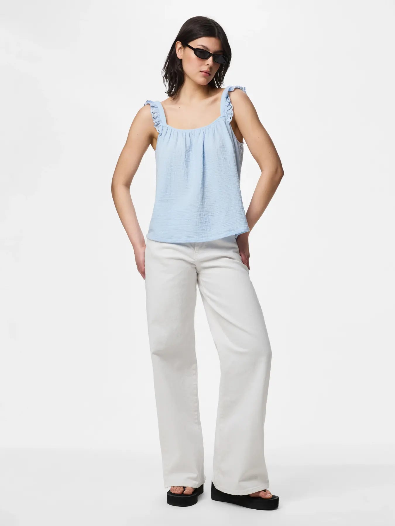 Woman wearing a light blue sleeveless top and white pants on a white background