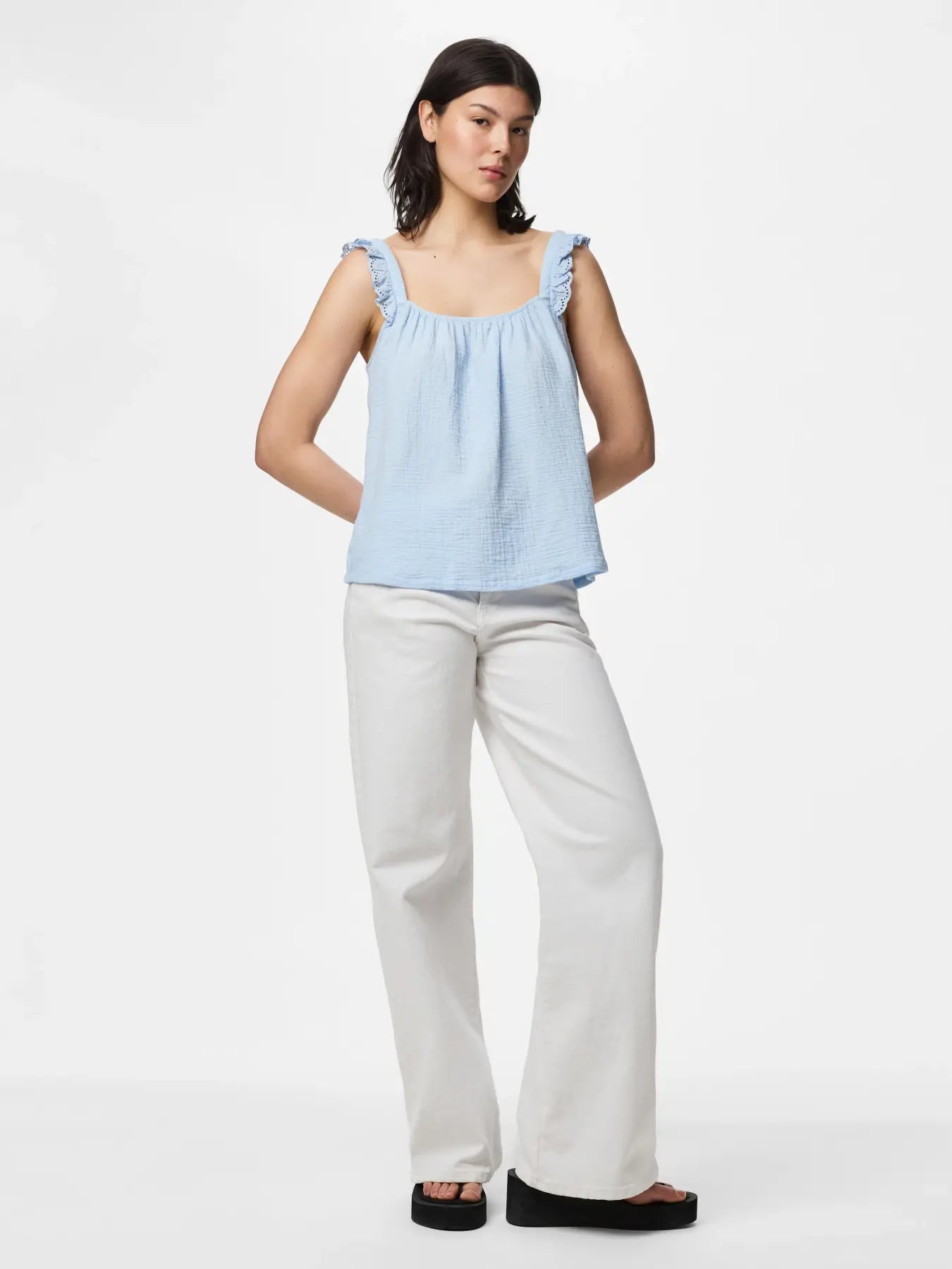 Woman wearing a light blue top and white pants on a white background