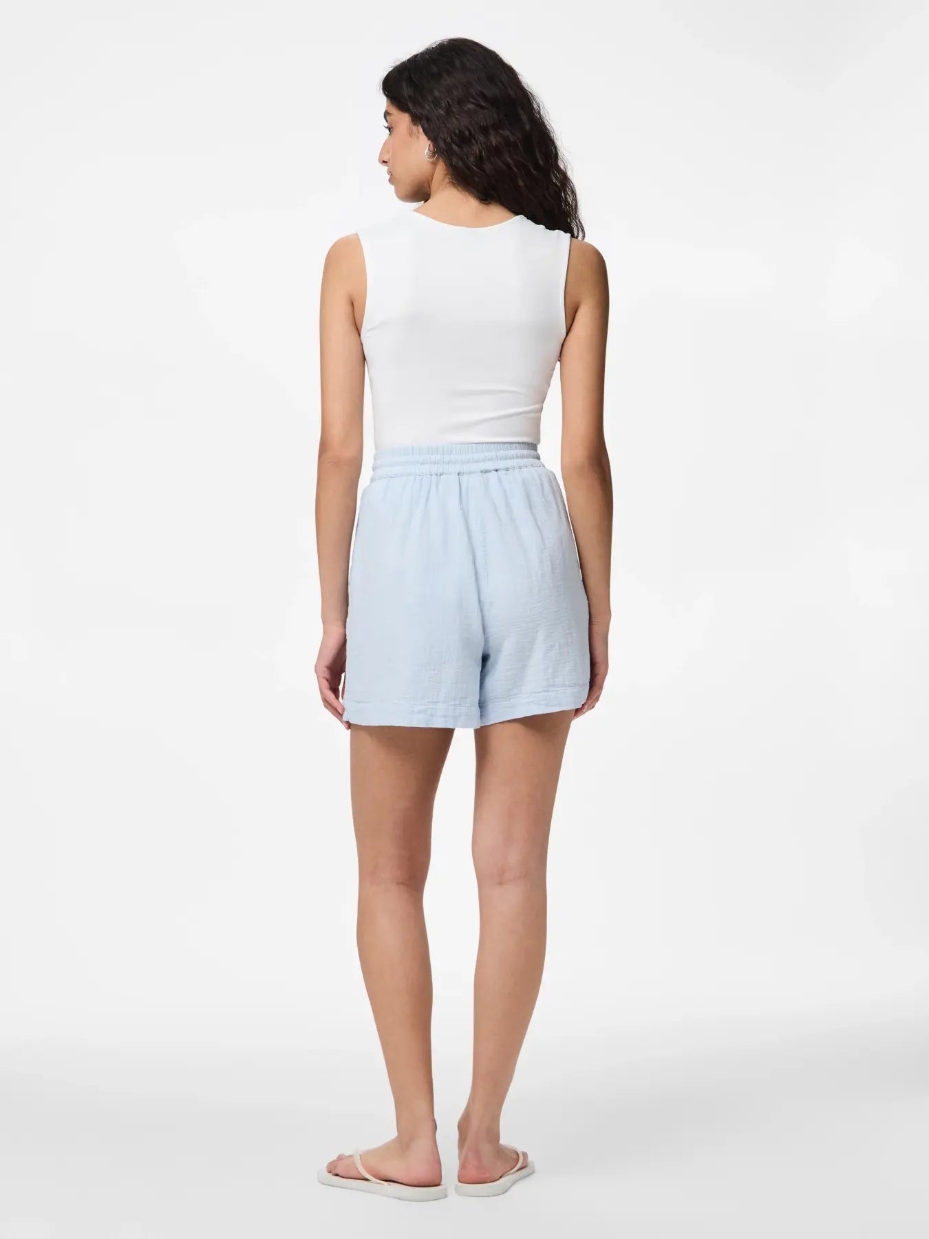 Woman wearing light blue shorts and a white top on a white background