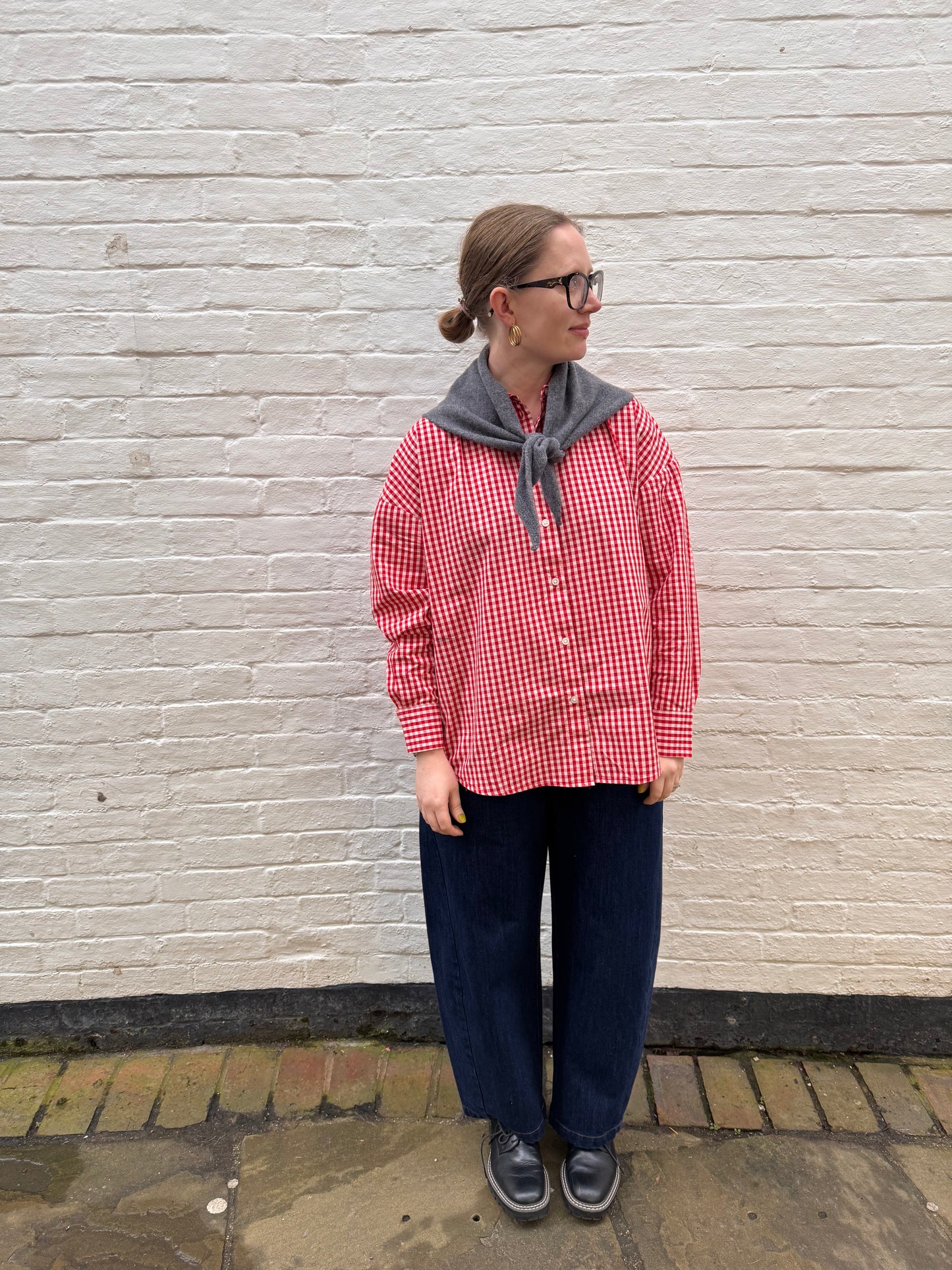 Person wearing a red and white checkered shirt and blue pants against a white brick wall.