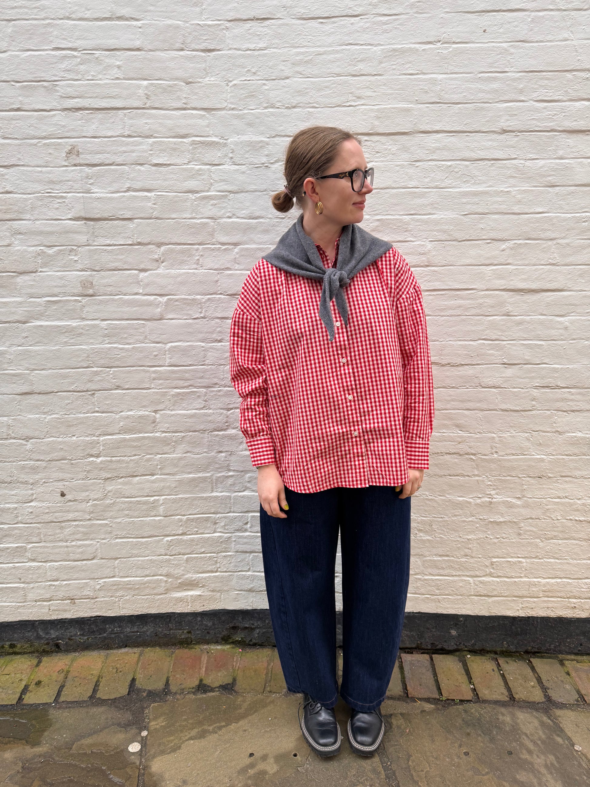 Person wearing a red and white checkered shirt and blue pants against a white brick wall.