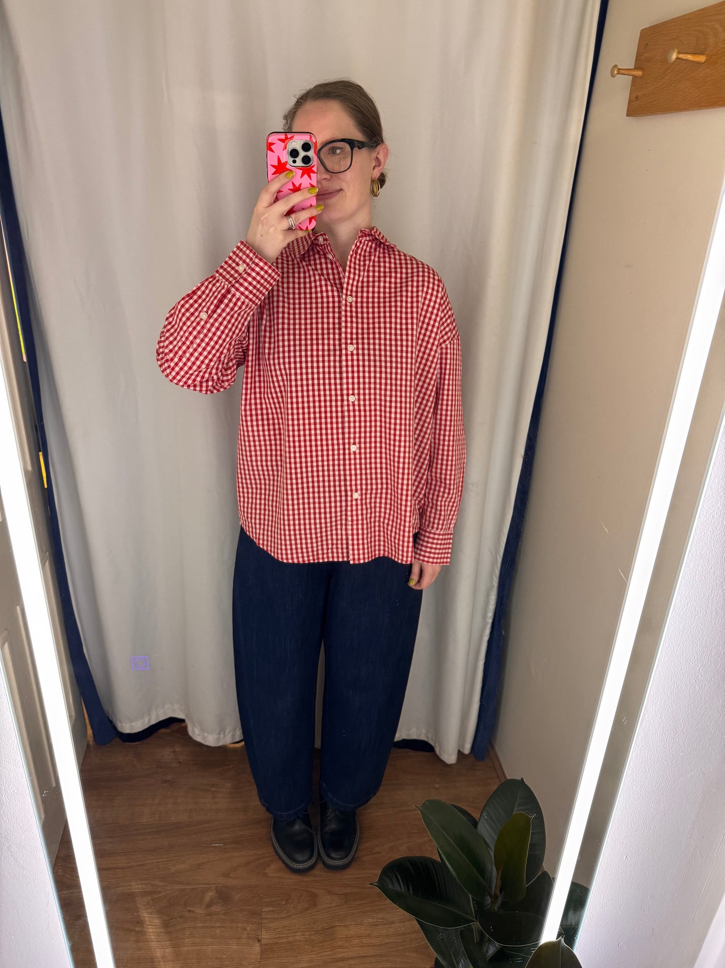 Person wearing a red and white checkered shirt and blue pants taking a mirror selfie.