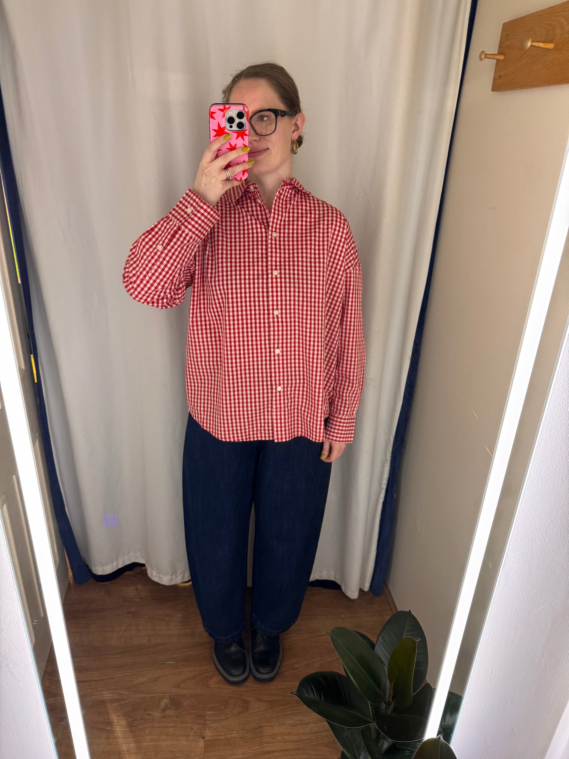 Person wearing a red and white checkered shirt and blue pants taking a mirror selfie.