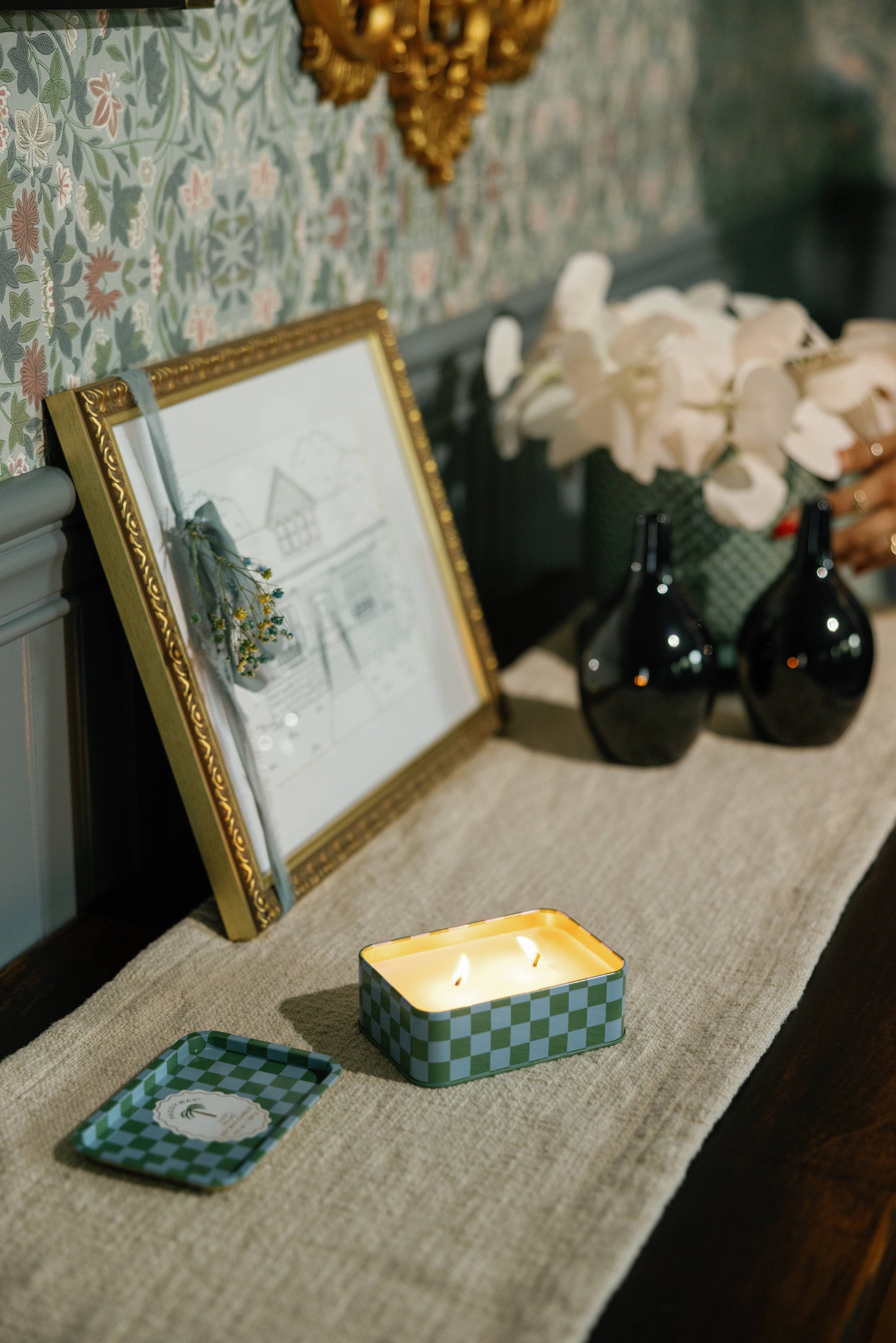 Decorative setting with a framed picture, candles, and vases on a surface.