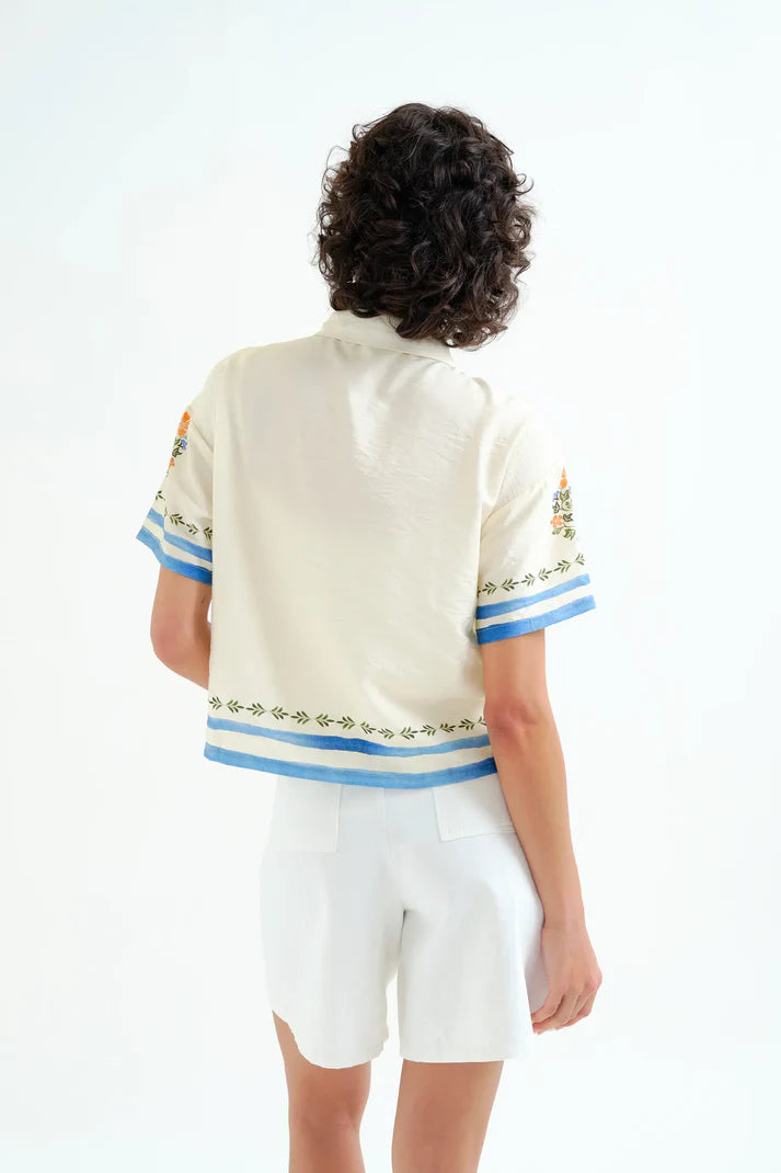 Person wearing a white blouse with blue and green embroidery on a white background