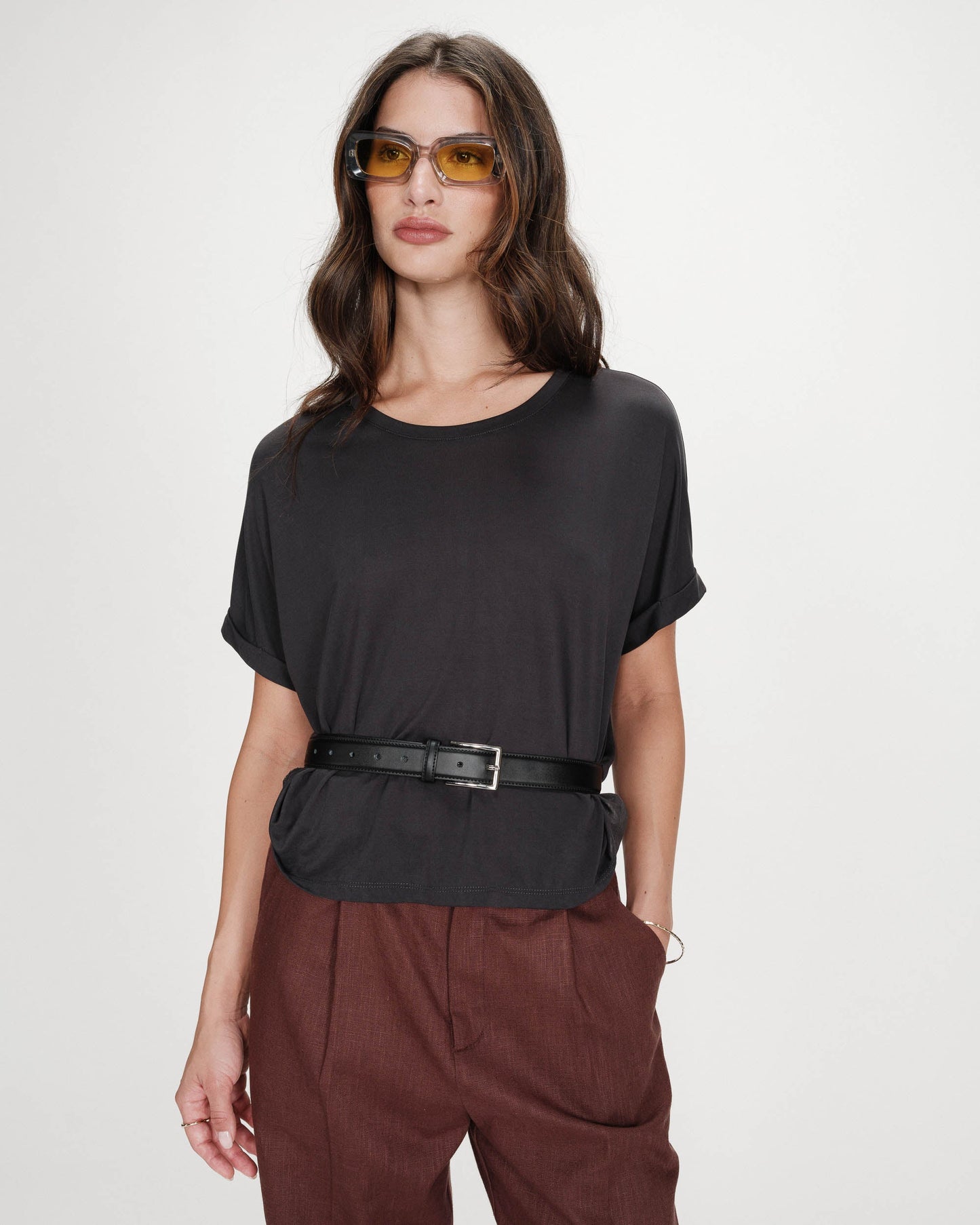 Woman wearing a black top and brown pants with sunglasses on a white background