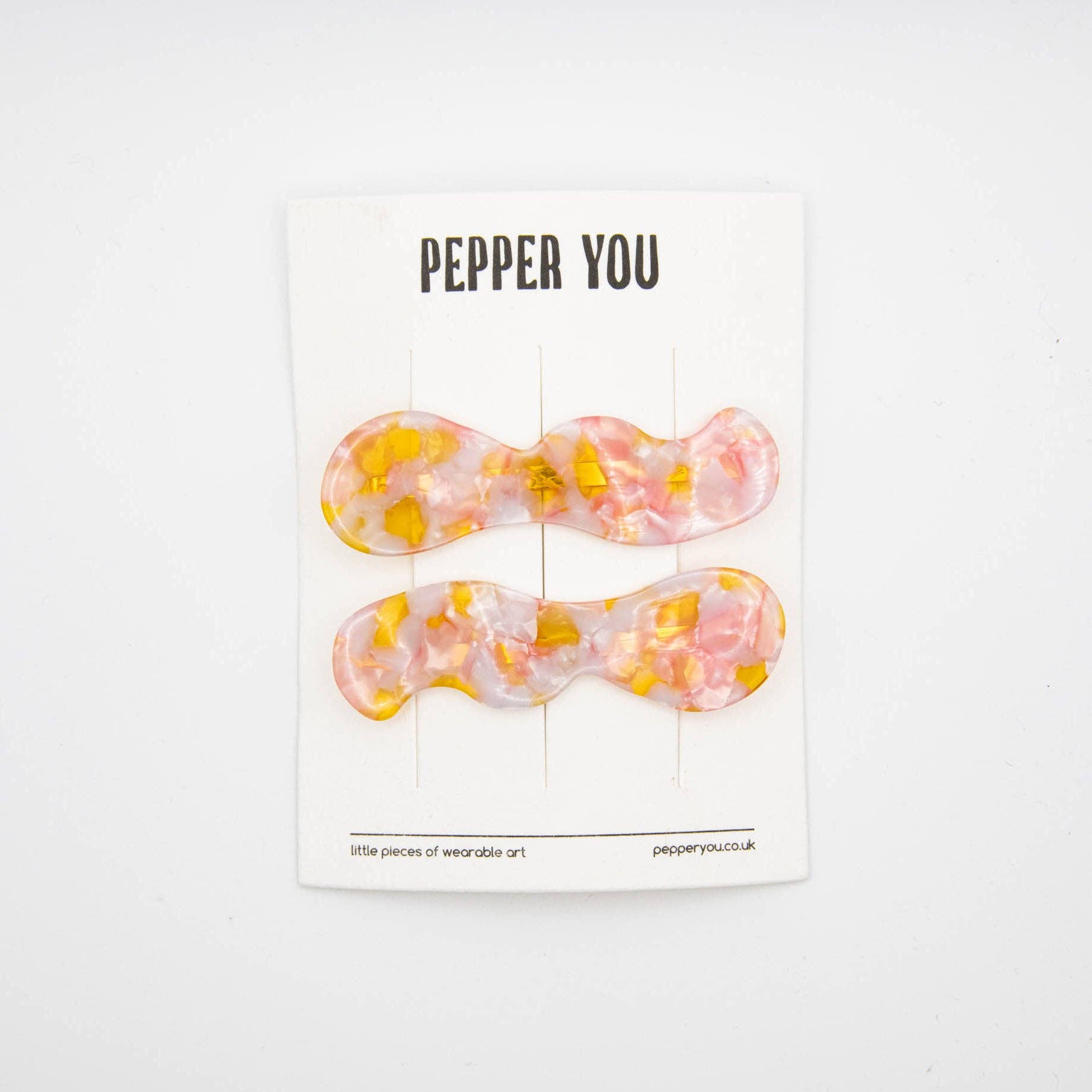 Two bow-shaped hair clips with a pink and yellow design on a 'PEPPER YOU' branded card.