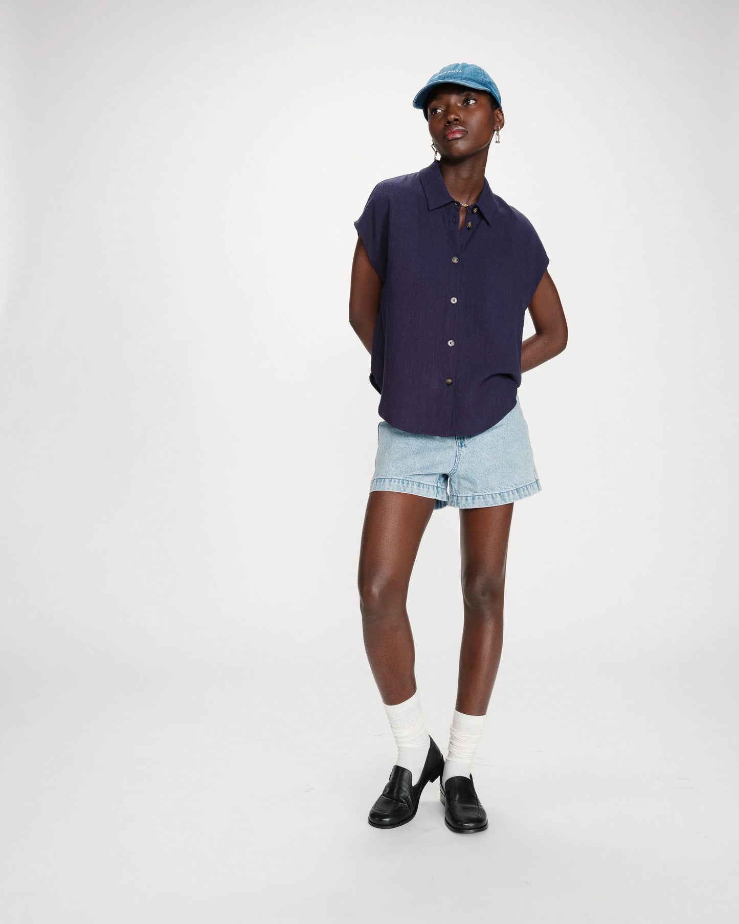 Person wearing a navy sleeveless shirt, light blue shorts, white socks, and black shoes on a white background