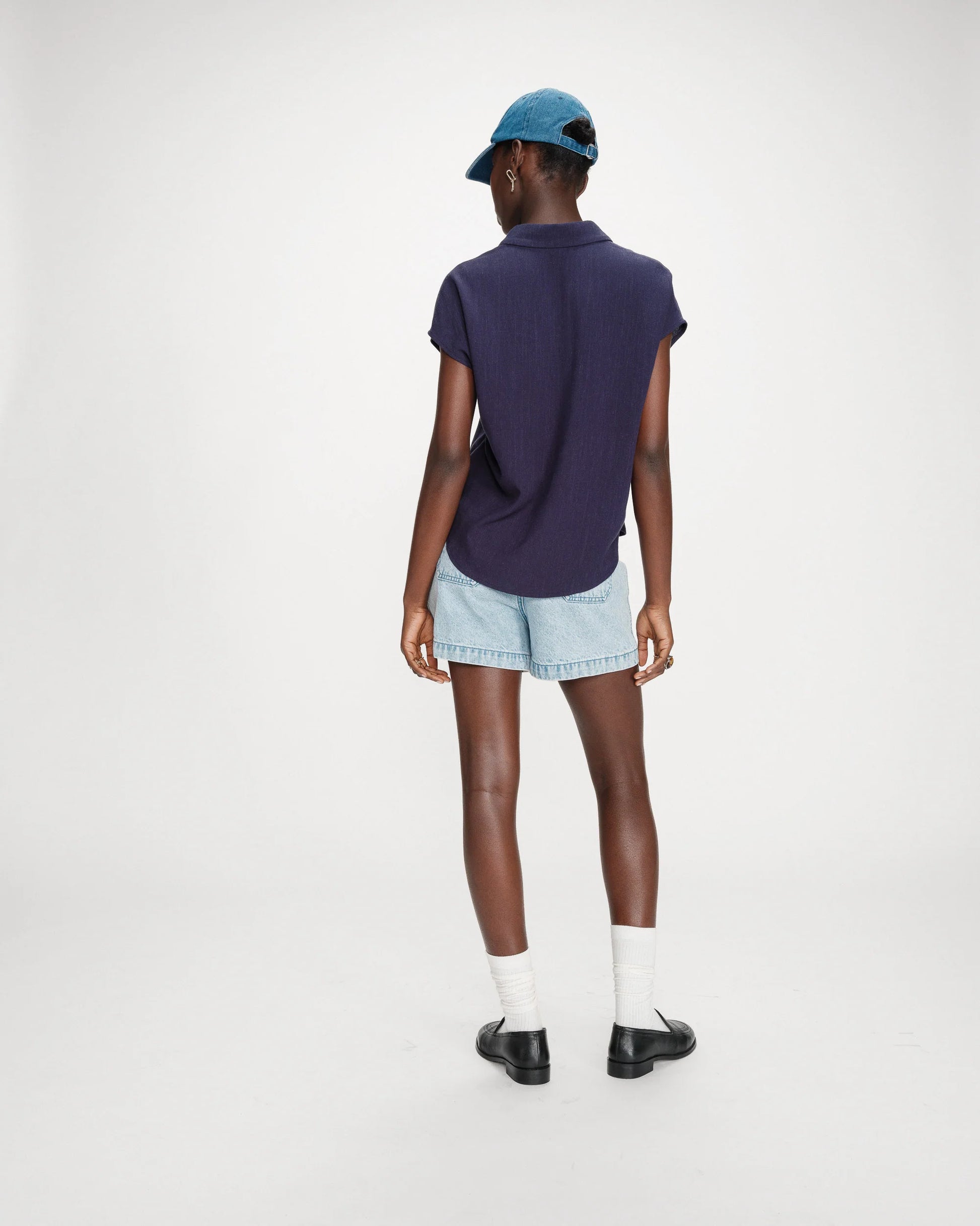 Person wearing a navy blue t-shirt, light blue shorts, and a blue cap on a white background