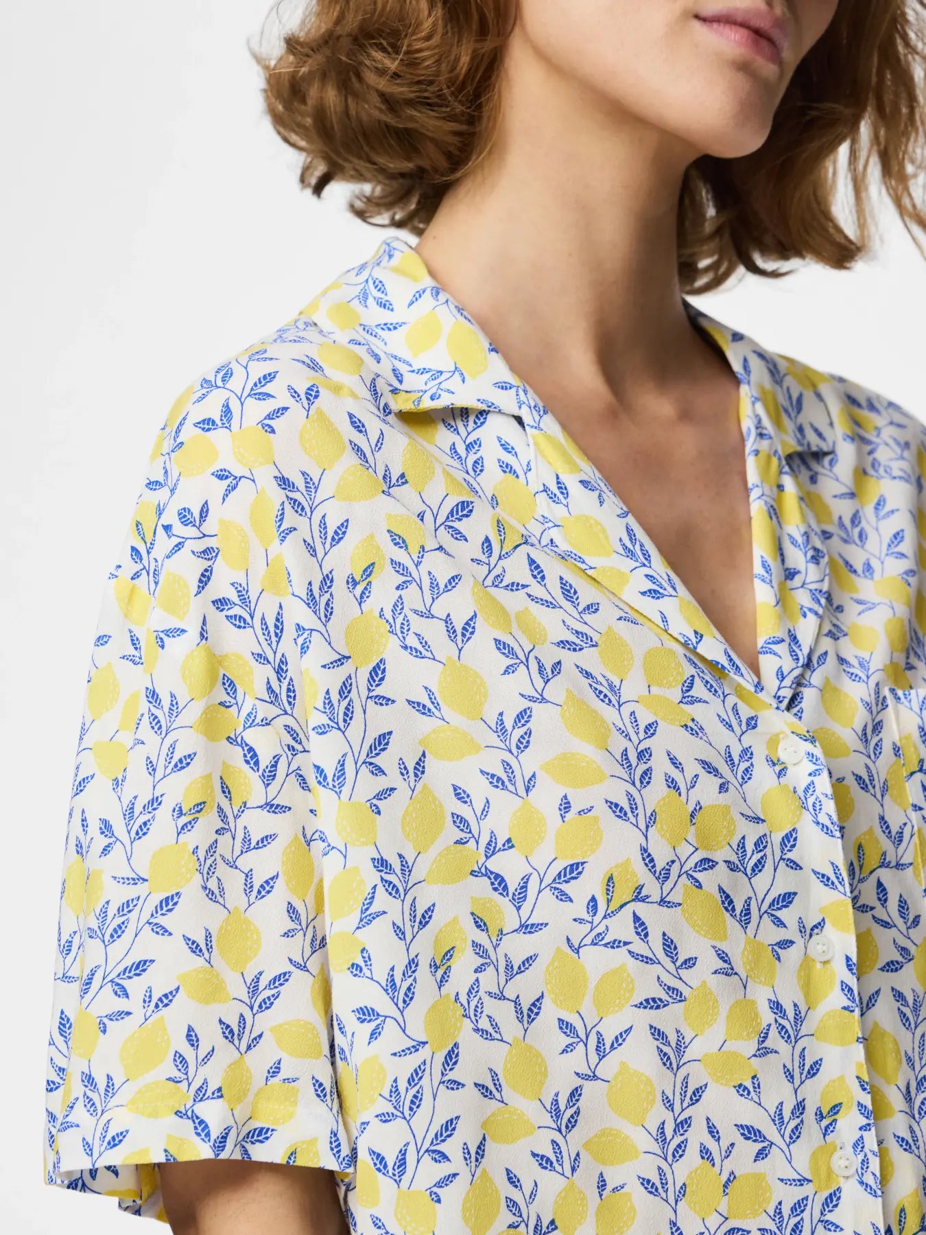Woman wearing a yellow and blue patterned blouse with a white background