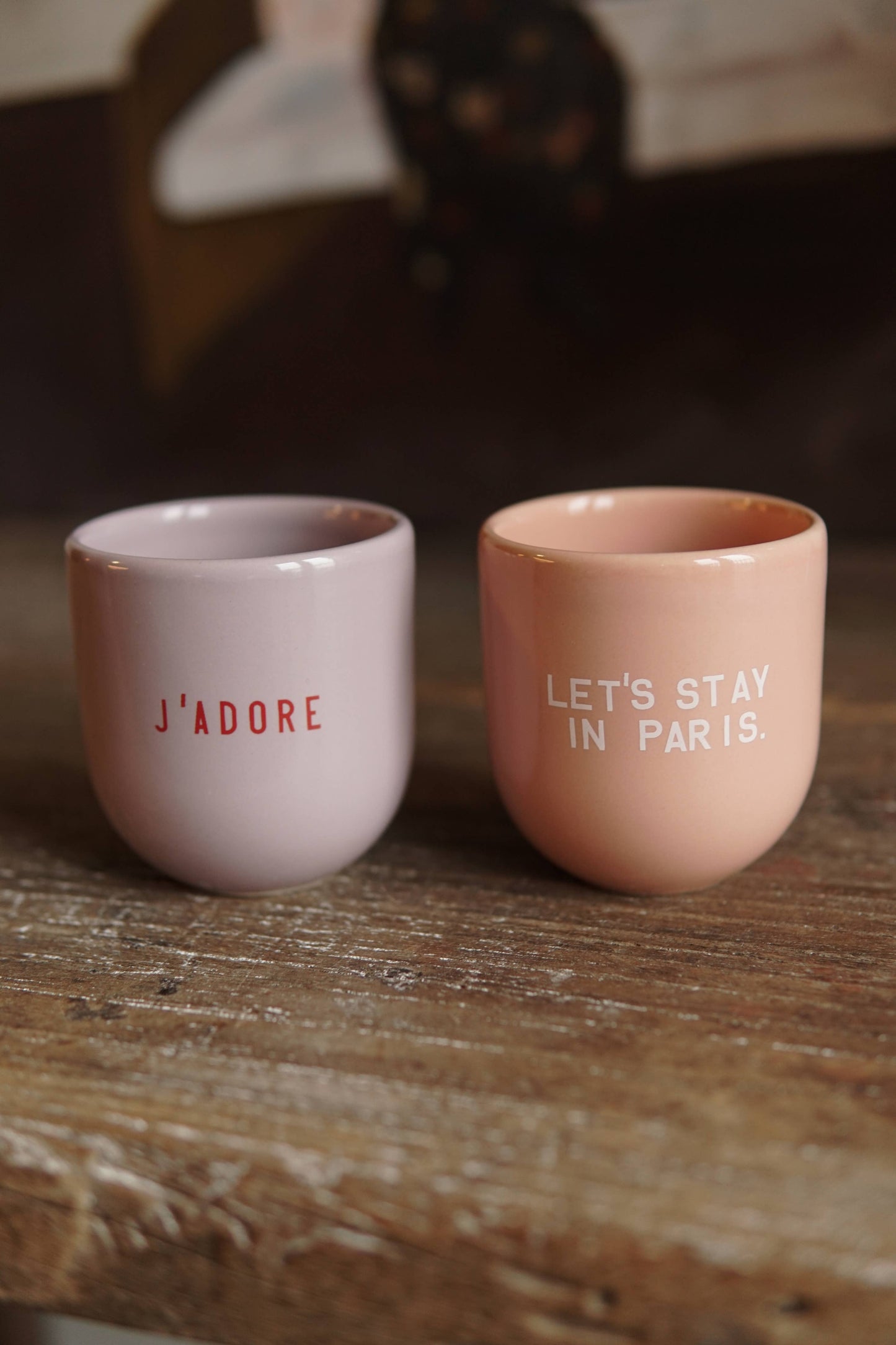 Two pink ceramic cups with text on a wooden surface