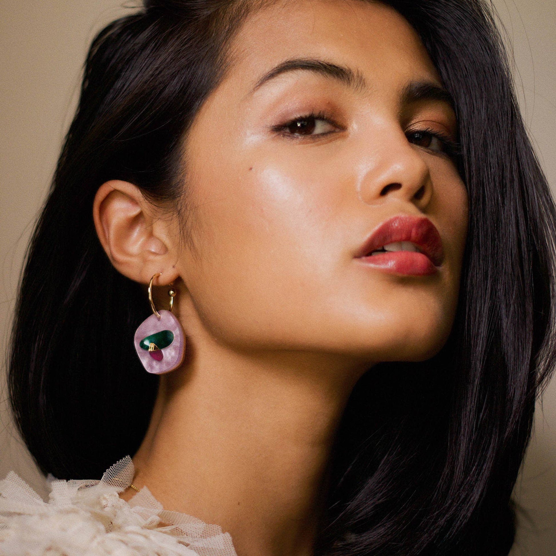 Close-up of a woman wearing colorful earrings with a neutral background