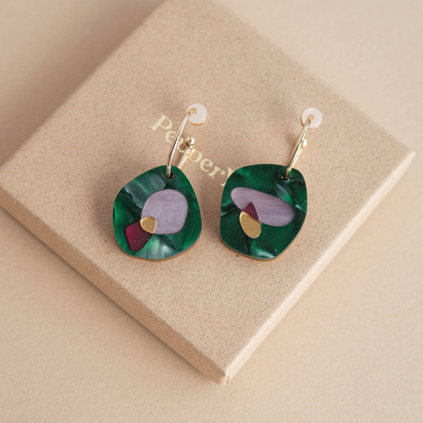 Green earrings with colorful accents on a beige jewelry box