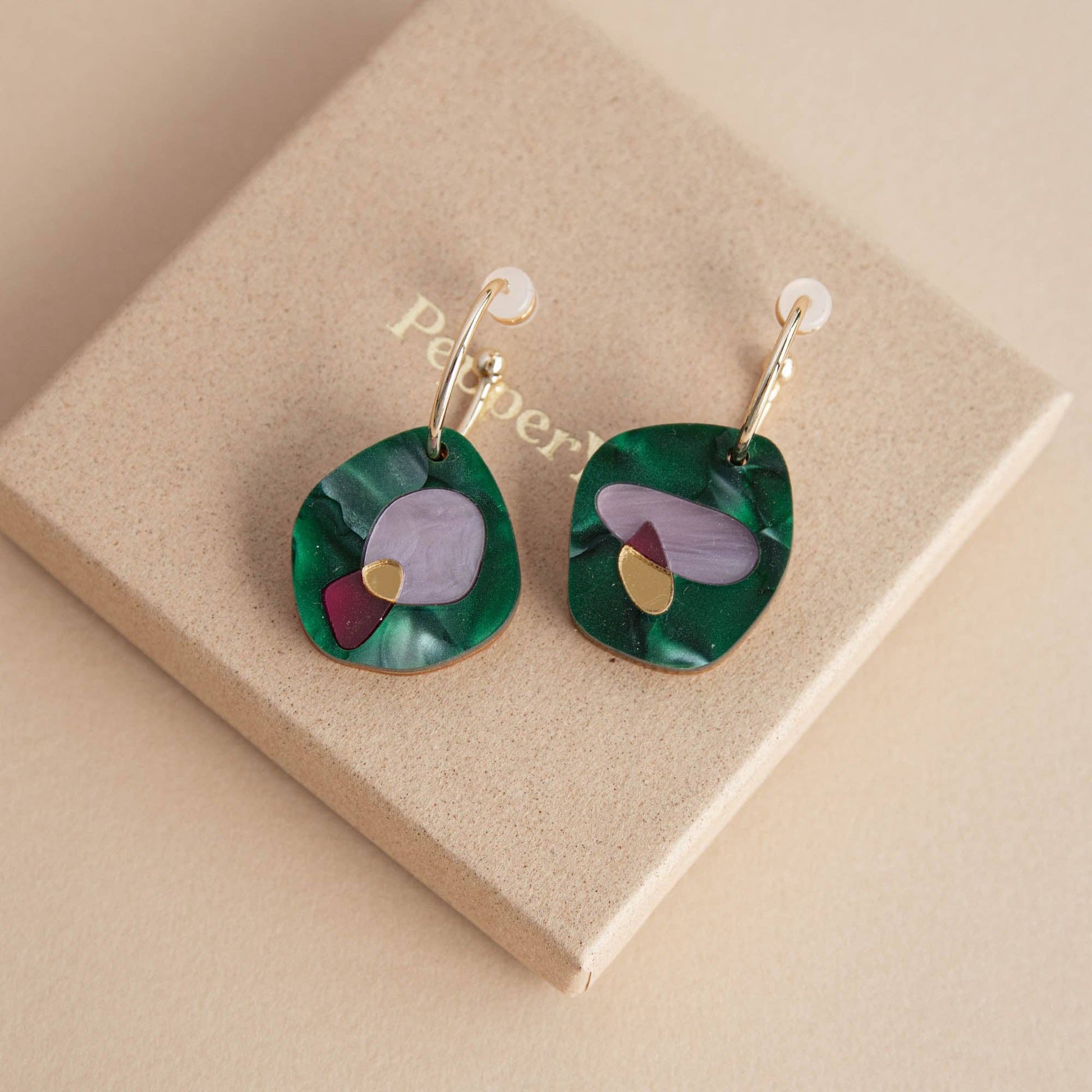 Green earrings with colorful accents on a beige jewelry box