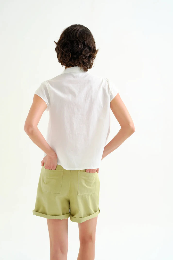 Person wearing a white shirt and light green shorts on a plain background