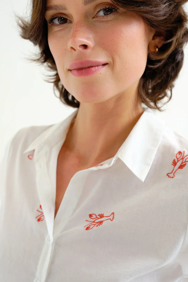 Woman wearing a white shirt with red floral embroidery on a plain background