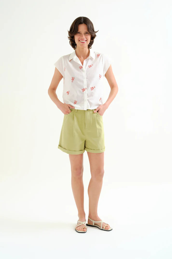 Woman wearing a white blouse with small patterns and light green shorts on a white background