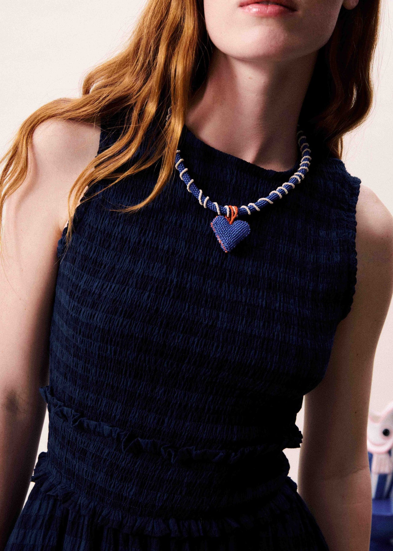 Woman wearing a dark blue textured dress with a colorful necklace featuring a heart pendant.