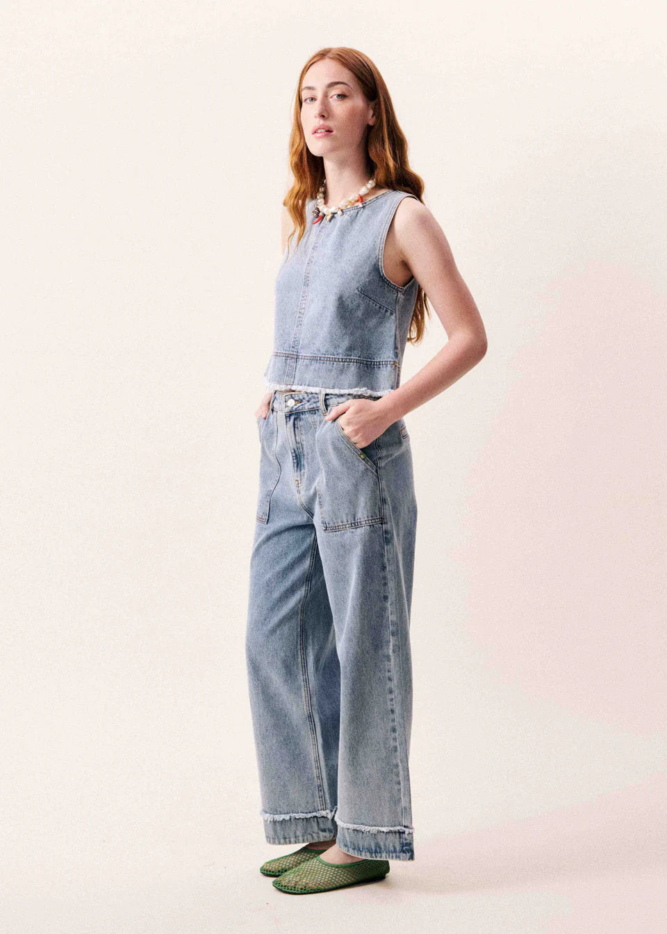 Woman wearing a denim sleeveless top and wide-leg jeans on a light background