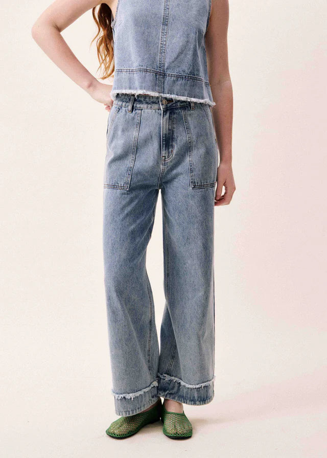 Person wearing light blue denim pants and a sleeveless denim top on a pink background