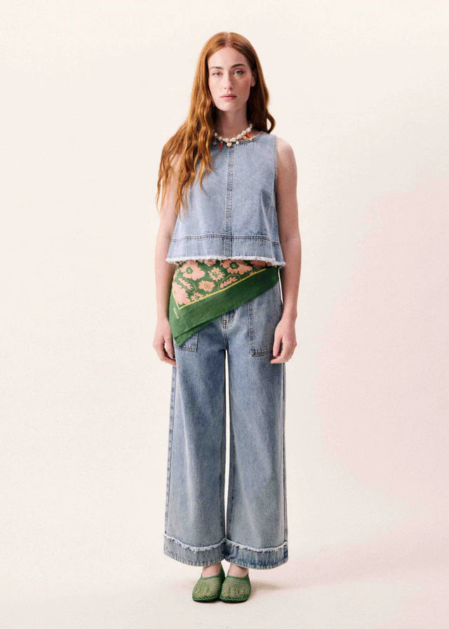 Woman wearing a denim top and wide-leg jeans with a green scarf on a light pink background