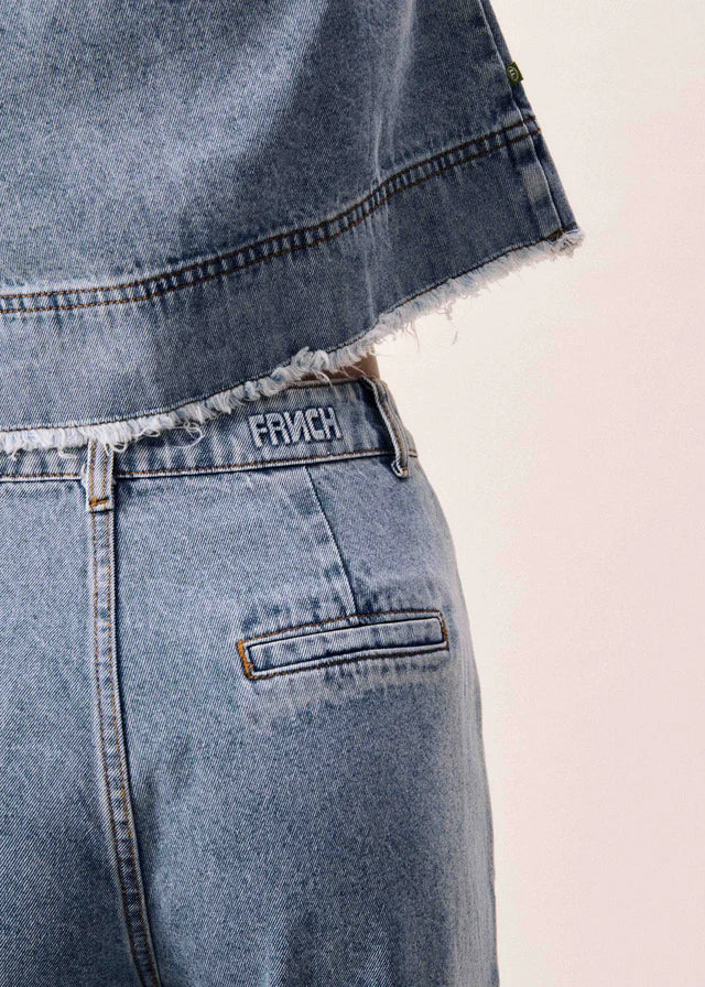 Close-up of a blue denim jacket with a brand logo on a light pink background