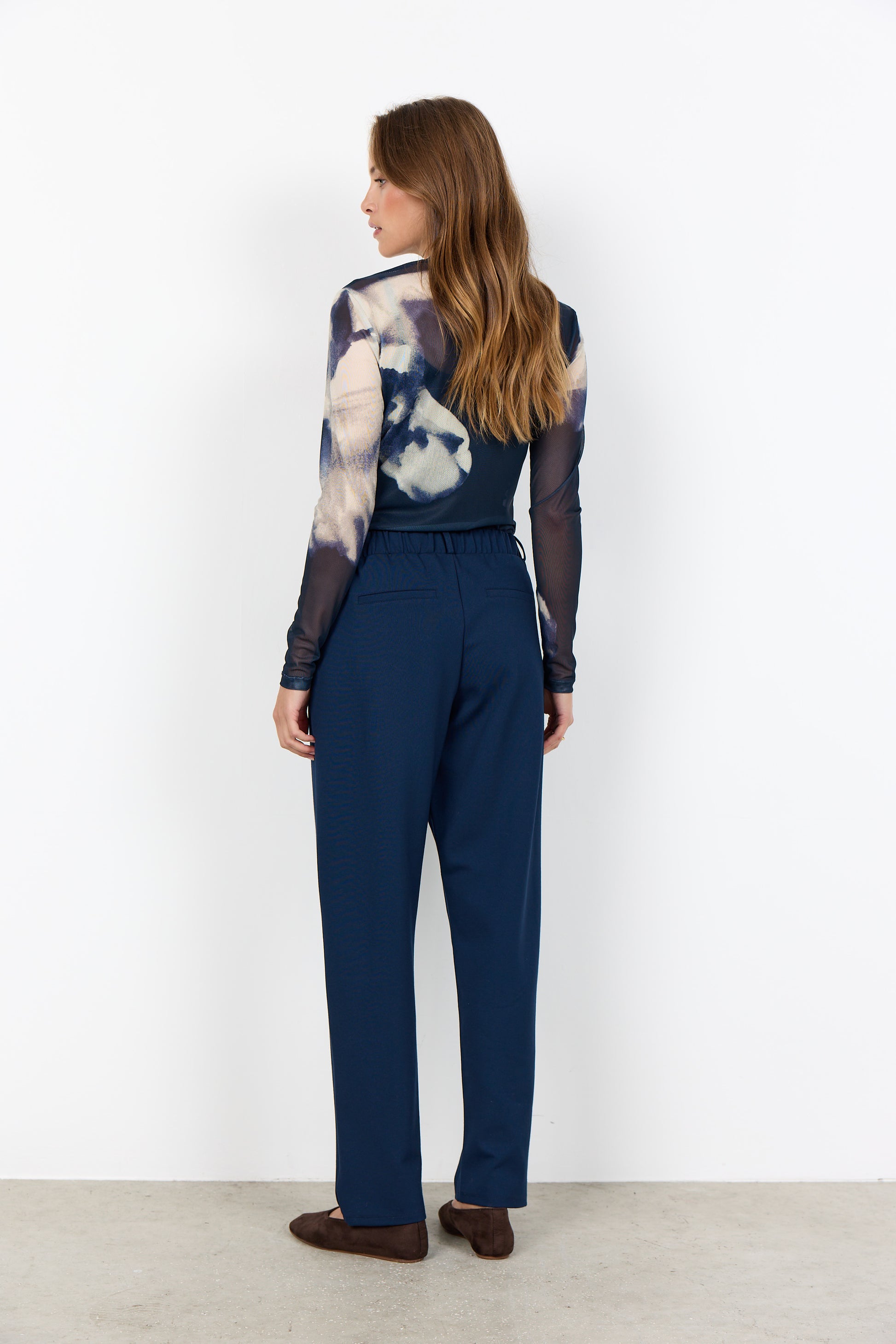 Woman wearing a patterned top and blue pants against a white background