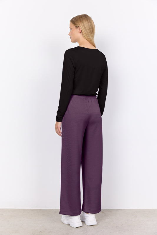 Woman wearing a black long-sleeve top and purple pants on a white background