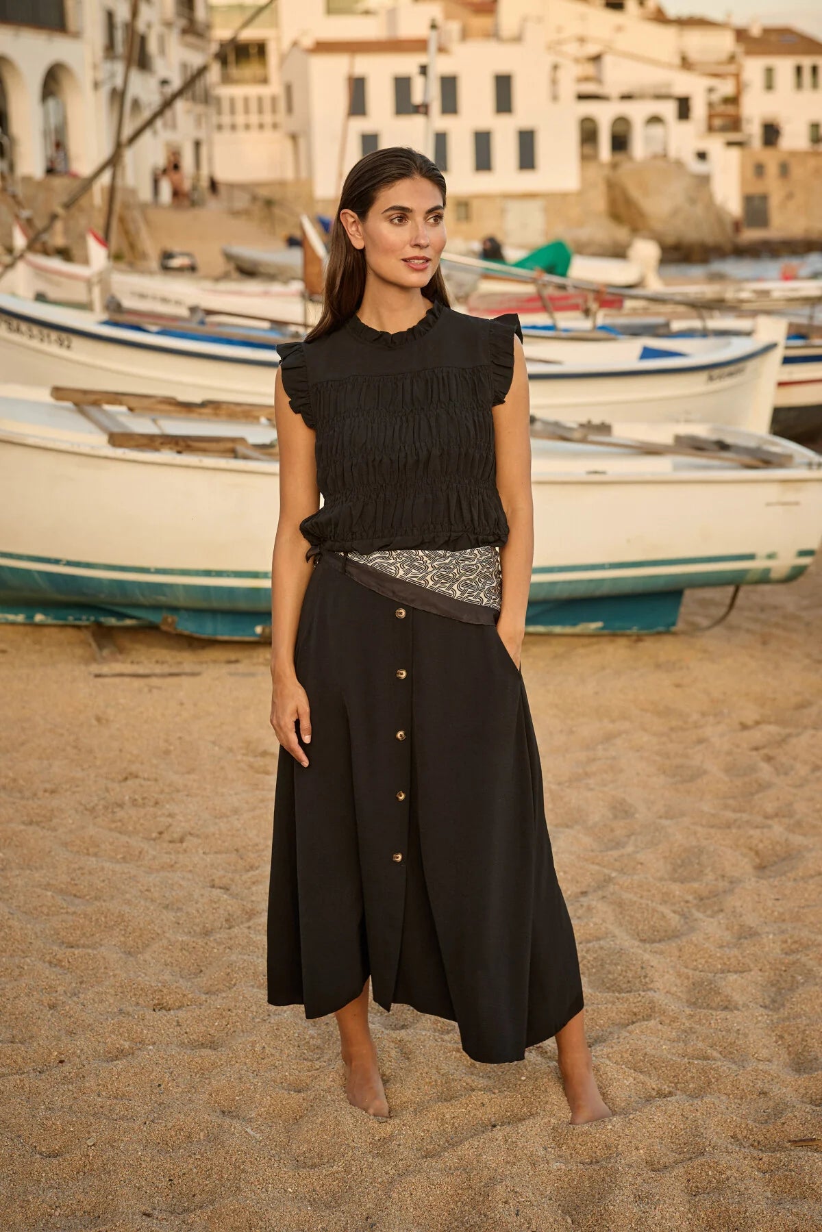 Woman in a black dress standing on a beach with boats in the background