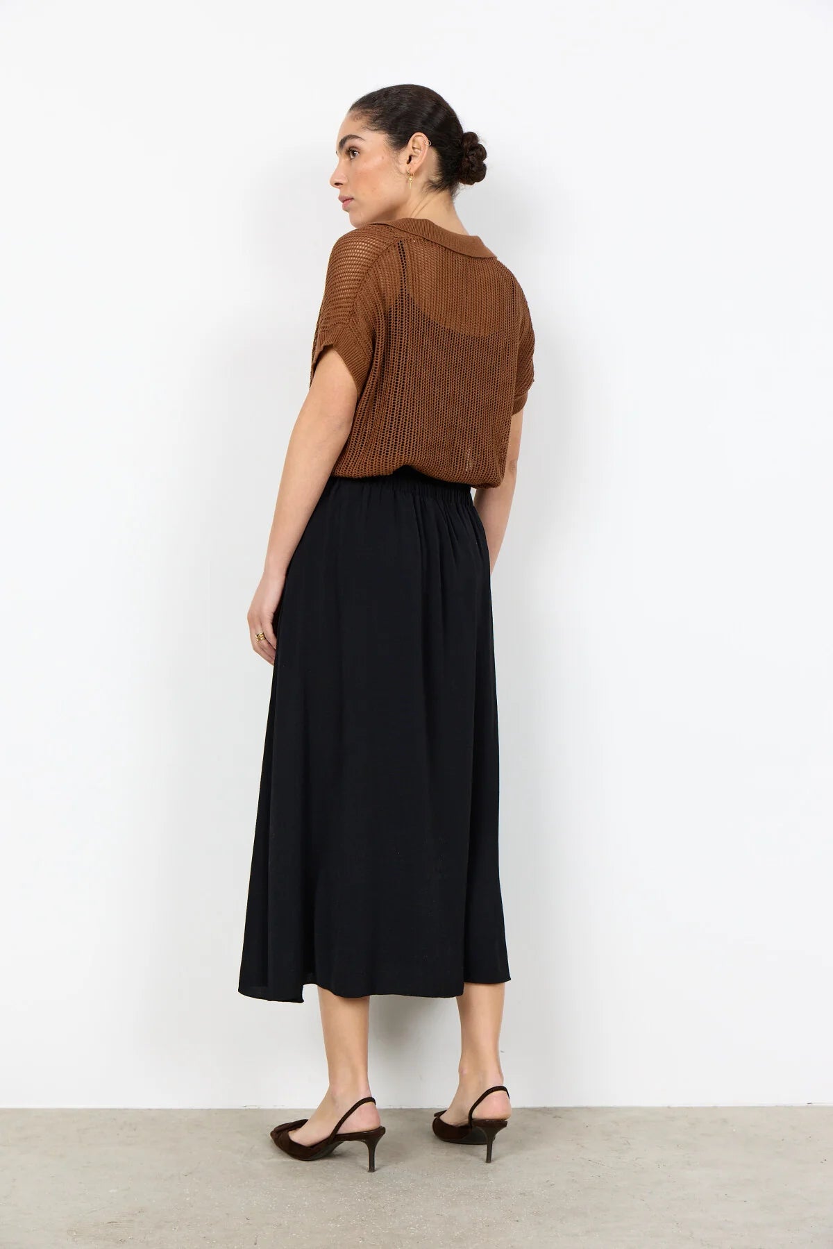 Woman wearing a brown cropped top and black skirt on a white background