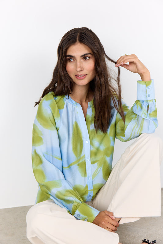 Woman wearing a green and blue tie-dye shirt sitting on a white couch.