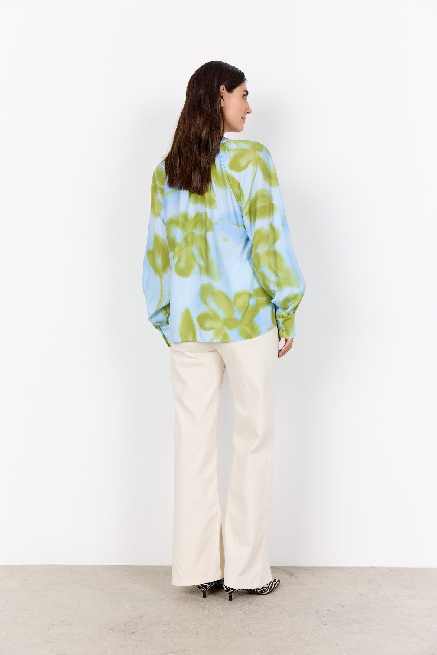 Woman wearing a colorful floral blouse and white pants against a white background
