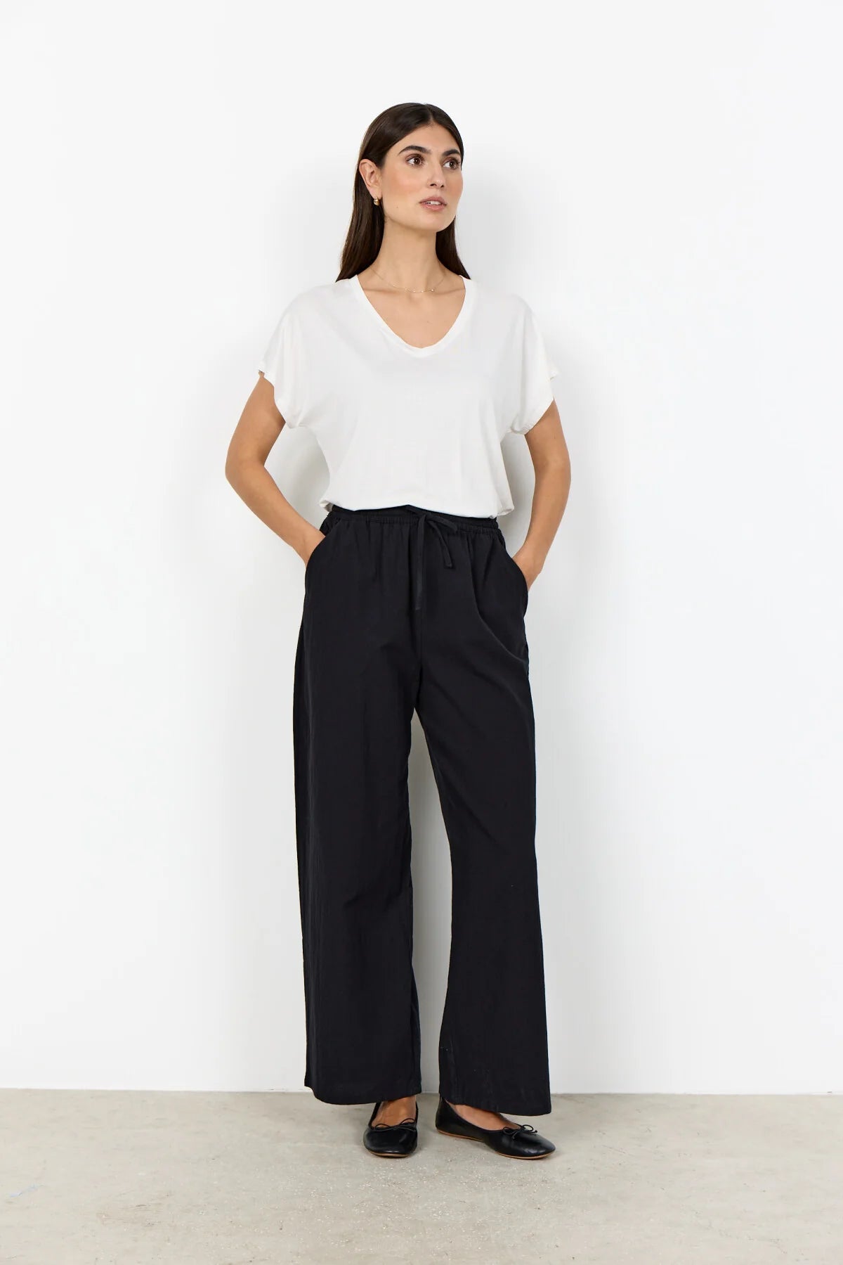 Woman wearing a white top and black pants against a white background