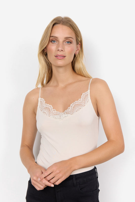 Woman wearing a white lace-trimmed tank top against a plain background