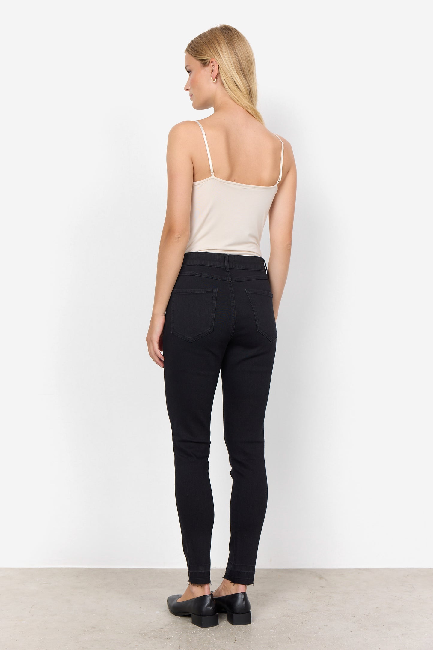 Woman wearing black pants and a beige top against a white background