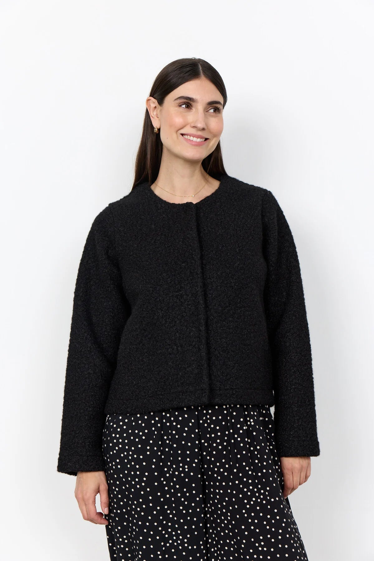 Woman wearing a black jacket and polka dot skirt on a neutral background
