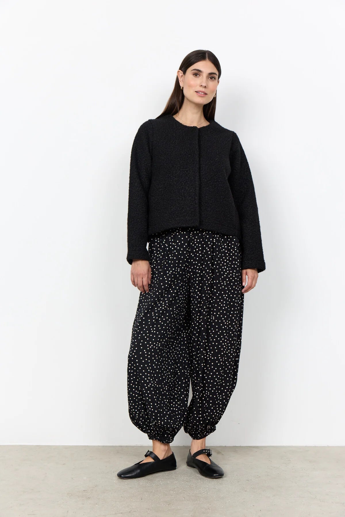 Woman wearing a black jacket and polka dot skirt on a neutral background