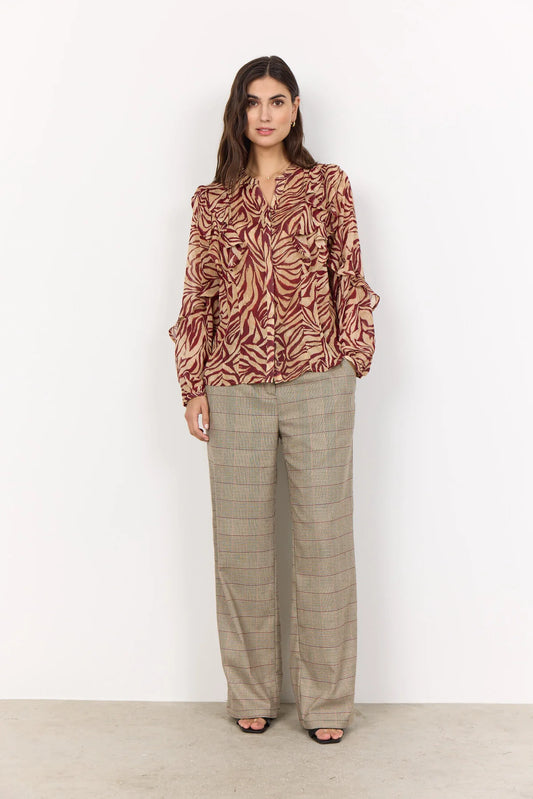Woman wearing a patterned blouse and beige pants against a white background