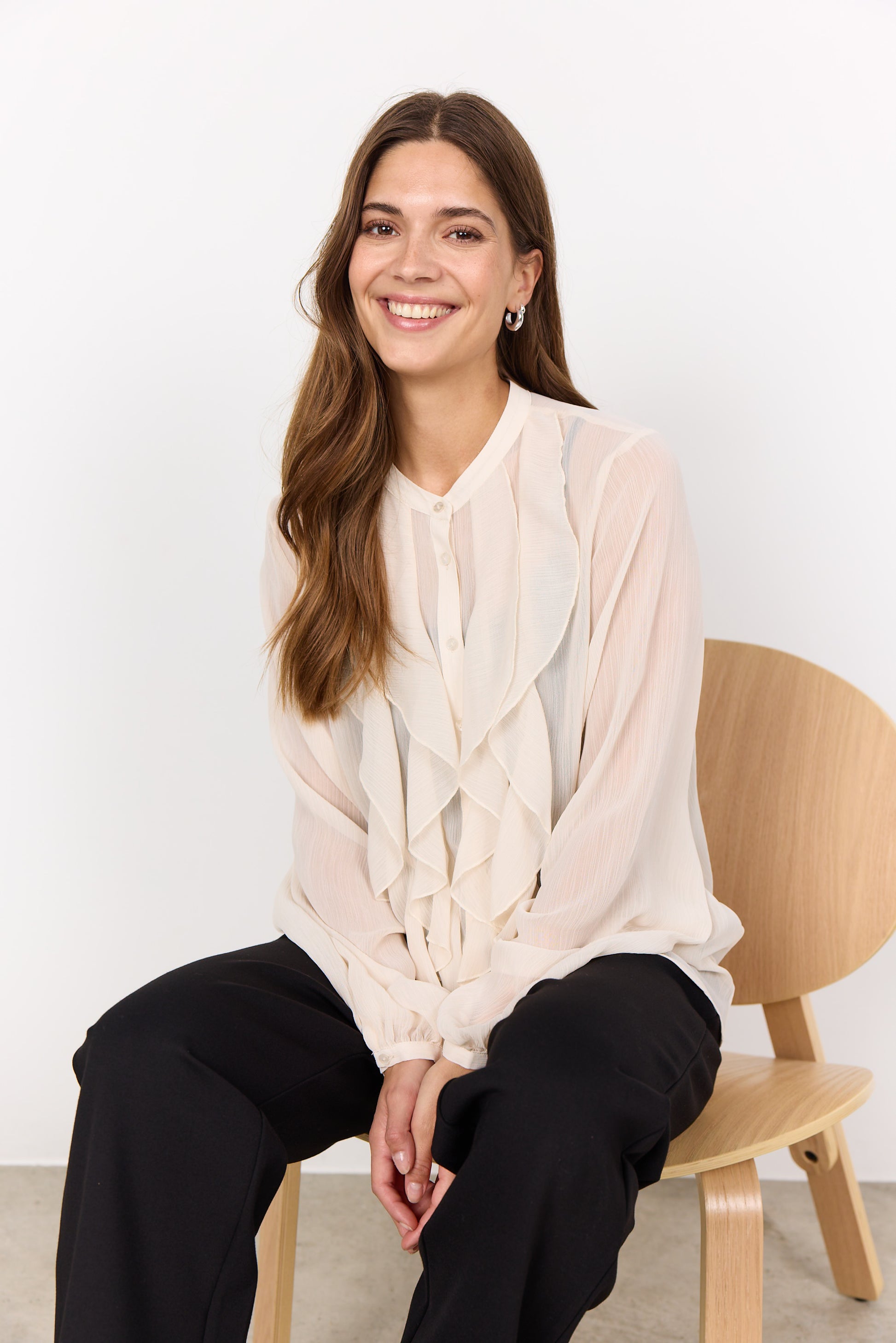 Woman sitting on a wooden chair wearing a light-colored blouse with a white background