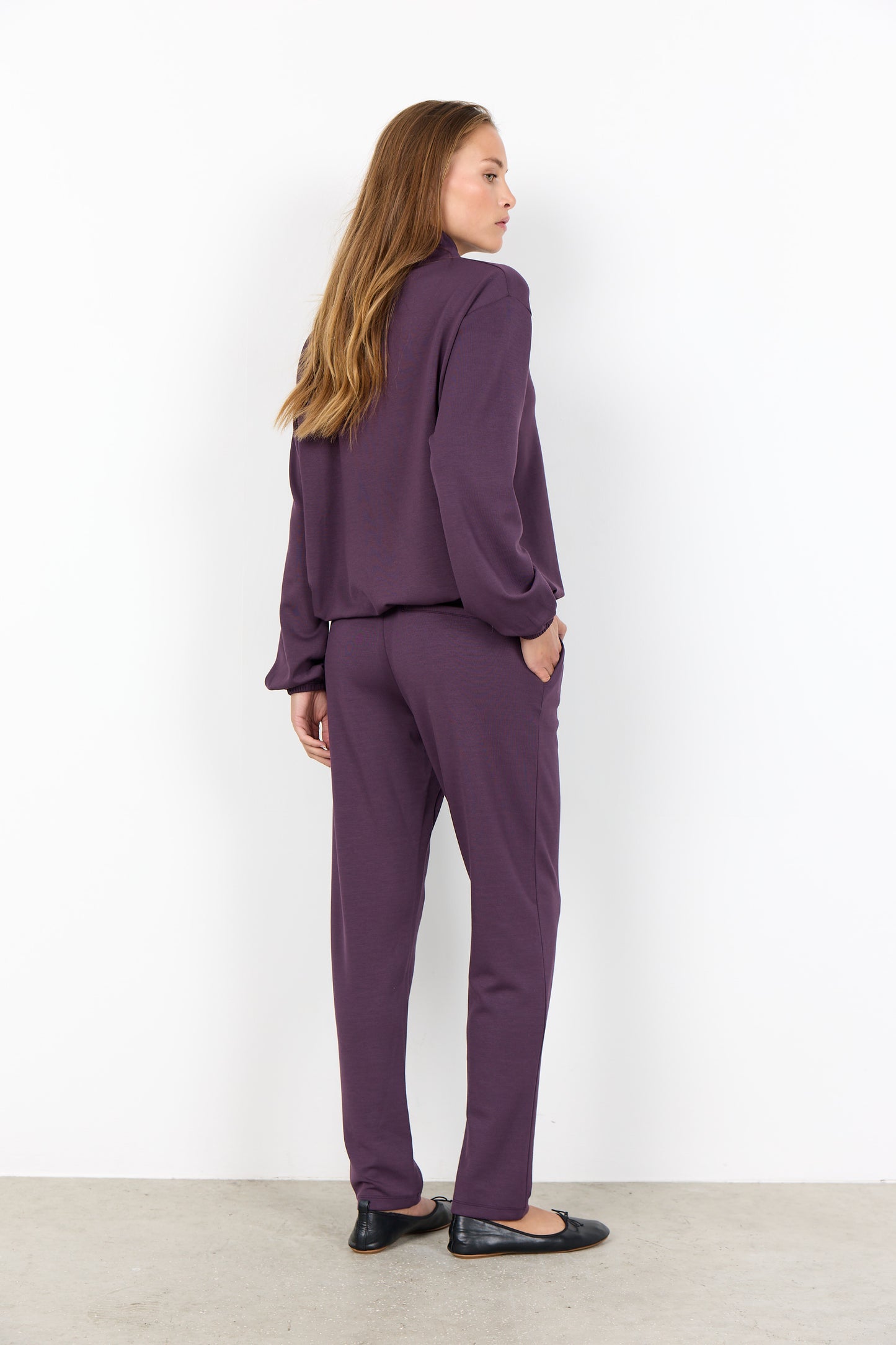 Woman wearing a purple suit standing against a white wall